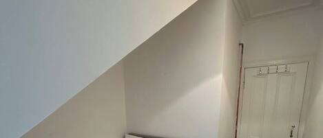 A small, neatly arranged bedroom with a single bed, a bedside table, and a door.