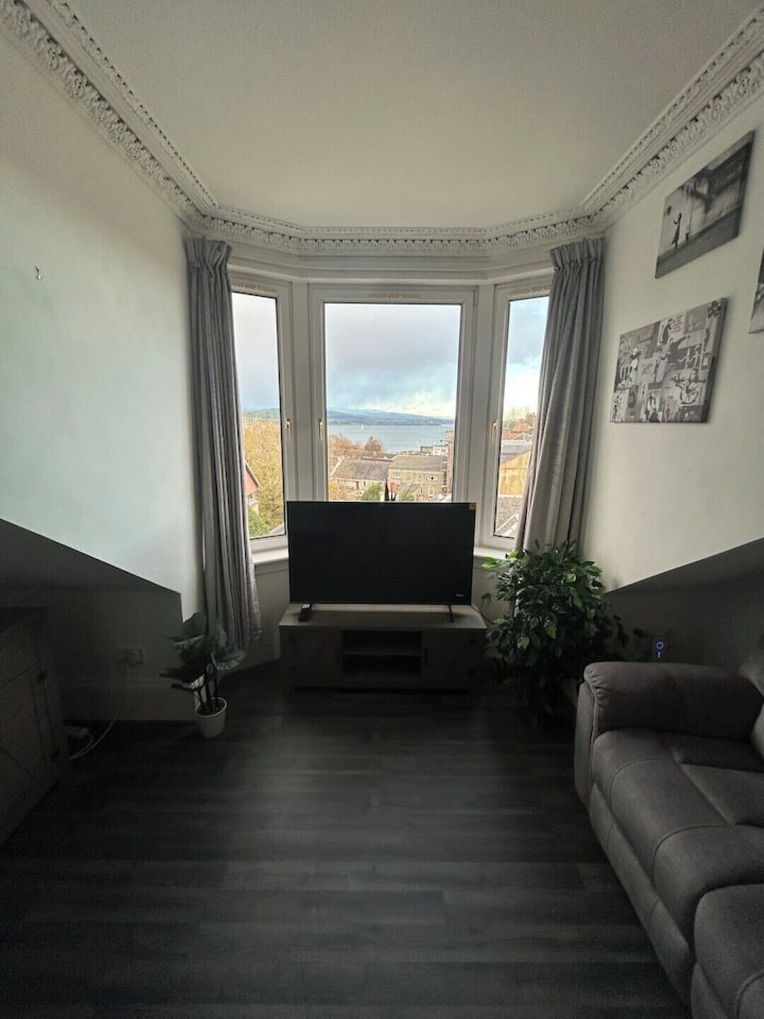 Ein Wohnzimmer mit großem Fenster, einem Flachbildfernseher, einer Couch und einem Blumentopf.