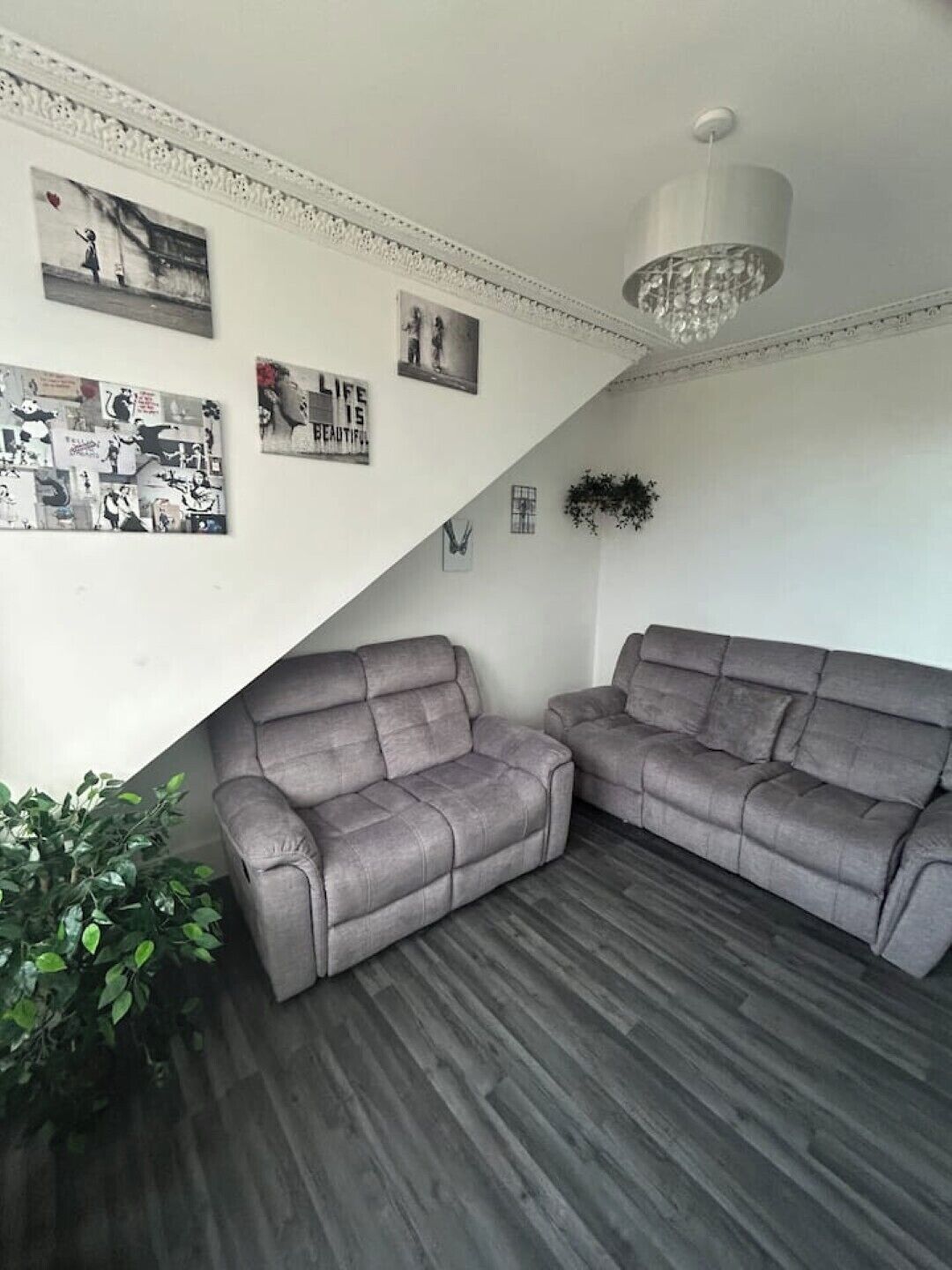 Een moderne woonkamer met twee grijze banken, een houten vloer en een kroonluchter.