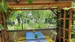 Un espace extérieur aménagé avec des sièges, protégé par un toit, comprenant une table et des chaises, et entouré d’une pergola en bois et d’une clôture en métal.