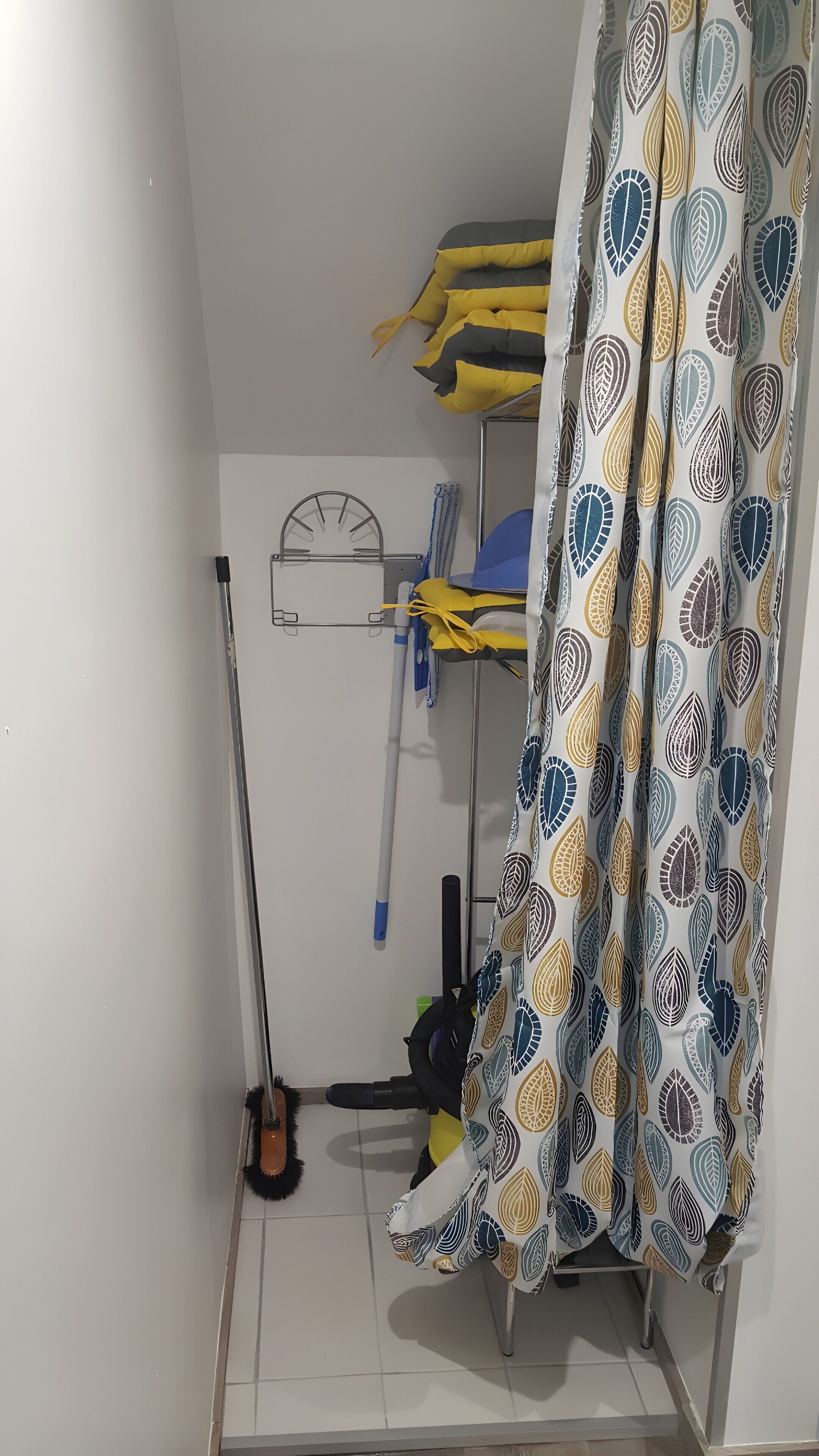 A room with a bunk bed, a standing fan, a broom, and a curtain with a leaf pattern.