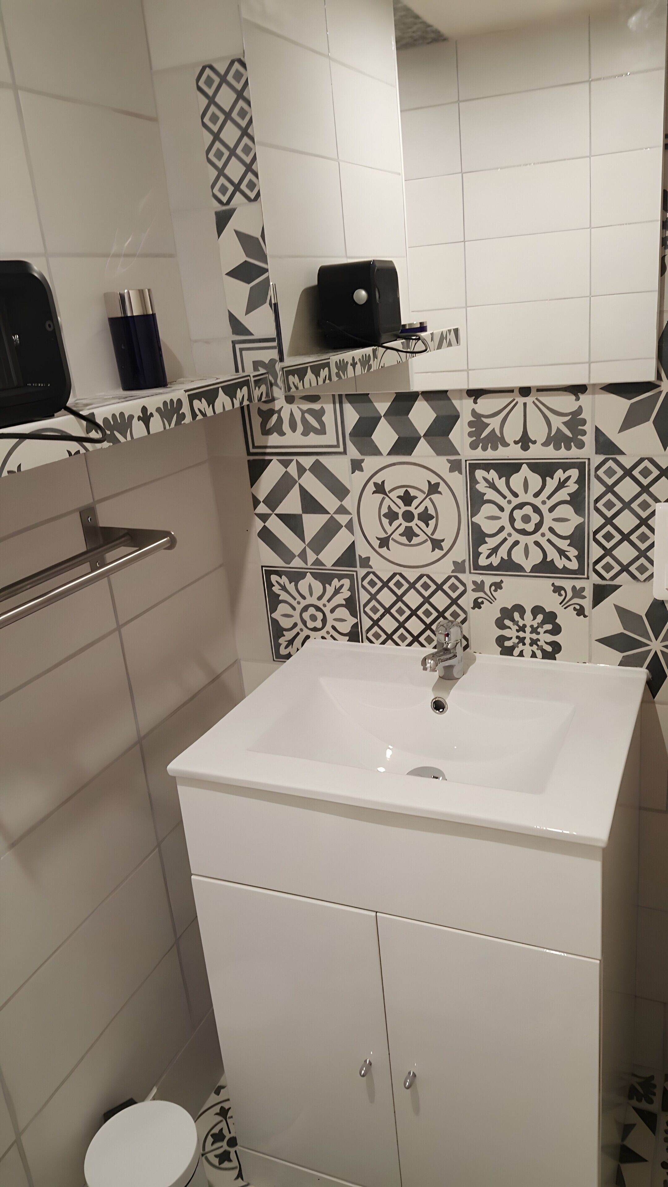 Ett badrum med ett vitt handfat, en spegel och mönstrade kakelplattor.