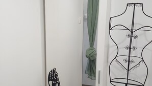 Un couloir étroit avec une porte blanche, une fresque représentant un Bouddha, un mannequin portant une robe et un ventilateur de plafond.