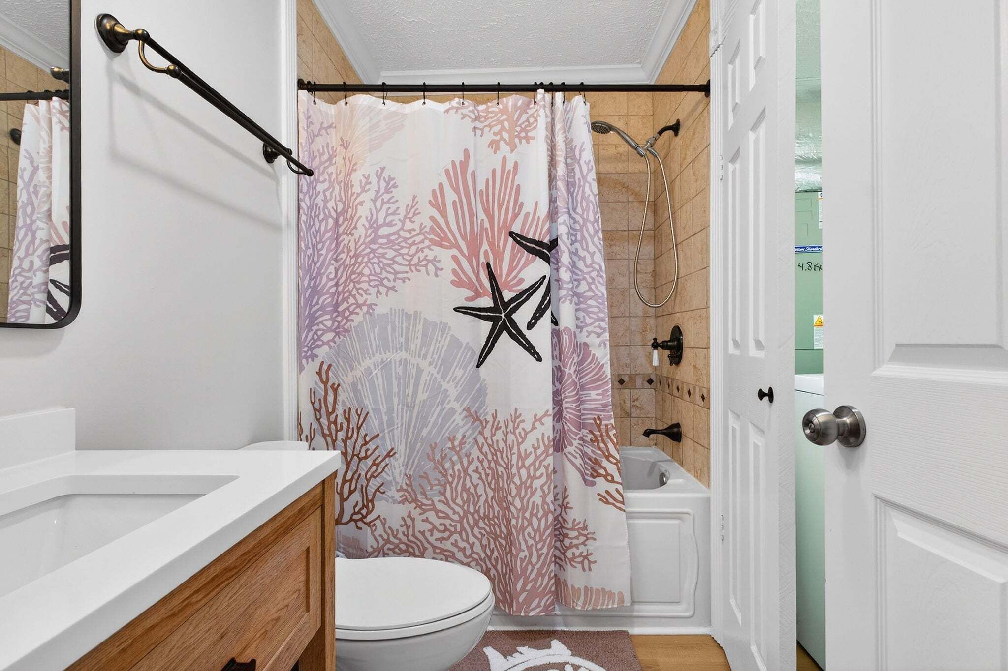 A bathroom with a shower curtain featuring coral and starfish patterns, a white sink, wooden cabinets, and a visible toilet.