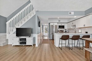 Eine moderne Küche mit weißen Schränken, einer zentralen Kochinsel mit Barhocker und einer Treppe mit weißen Geländern.