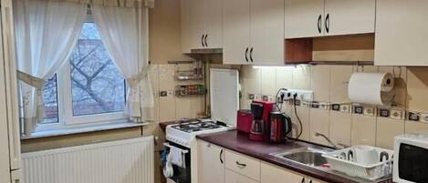 A kitchen with wooden cabinets, a stove, a sink, and a window with curtains.