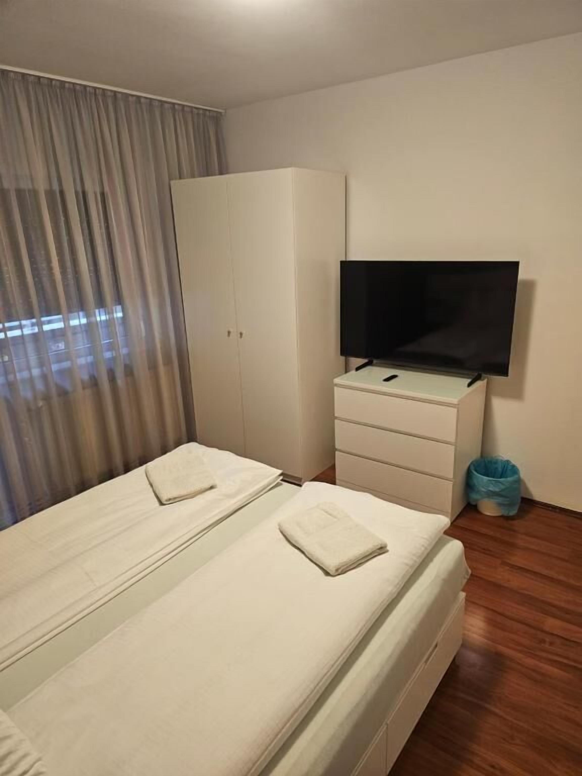 A hotel room with a bed, a TV, a wardrobe, and a window with curtains.