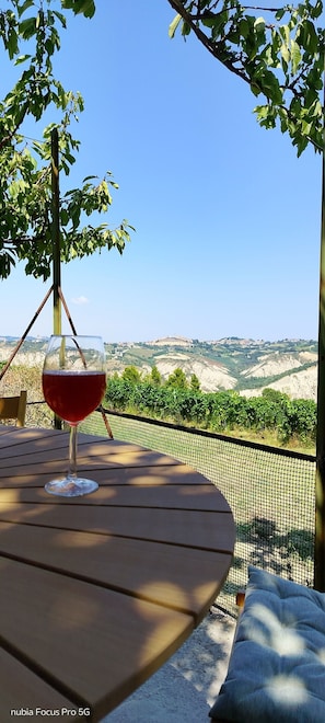 Een tafel met een wijnglas, uitzicht op een wijngaard en een helderblauwe lucht.