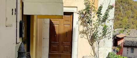 A courtyard with a stone floor, a bench, a potted plant, and a building entrance with a wooden door.