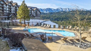 A resort with a pool, lounge chairs, and a view of snow-capped mountains.