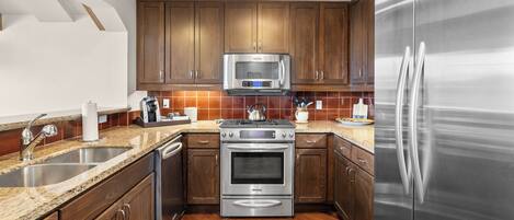 A modern kitchen with stainless steel appliances, wooden cabinets, and a granite countertop.