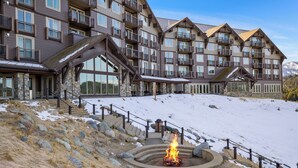 A multi-story hotel with balconies, a stone facade, and a snow-covered slope.