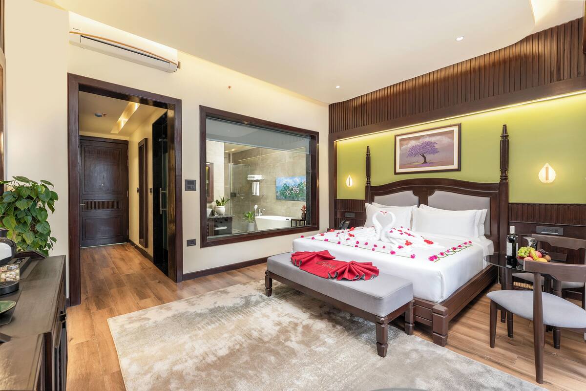 Habitación de hotel con una cama grande, zona de estar, vista al baño y una planta en maceta.