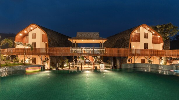 A large building with a swimming pool in front, a covered area with seating, and a staircase leading to an upper level. - Latauli Sanctuary (Kalika)