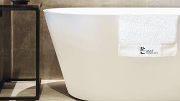 Un baño moderno con una bañera independiente, un cuadro de una escena boscosa y una mesita con una planta en maceta.
