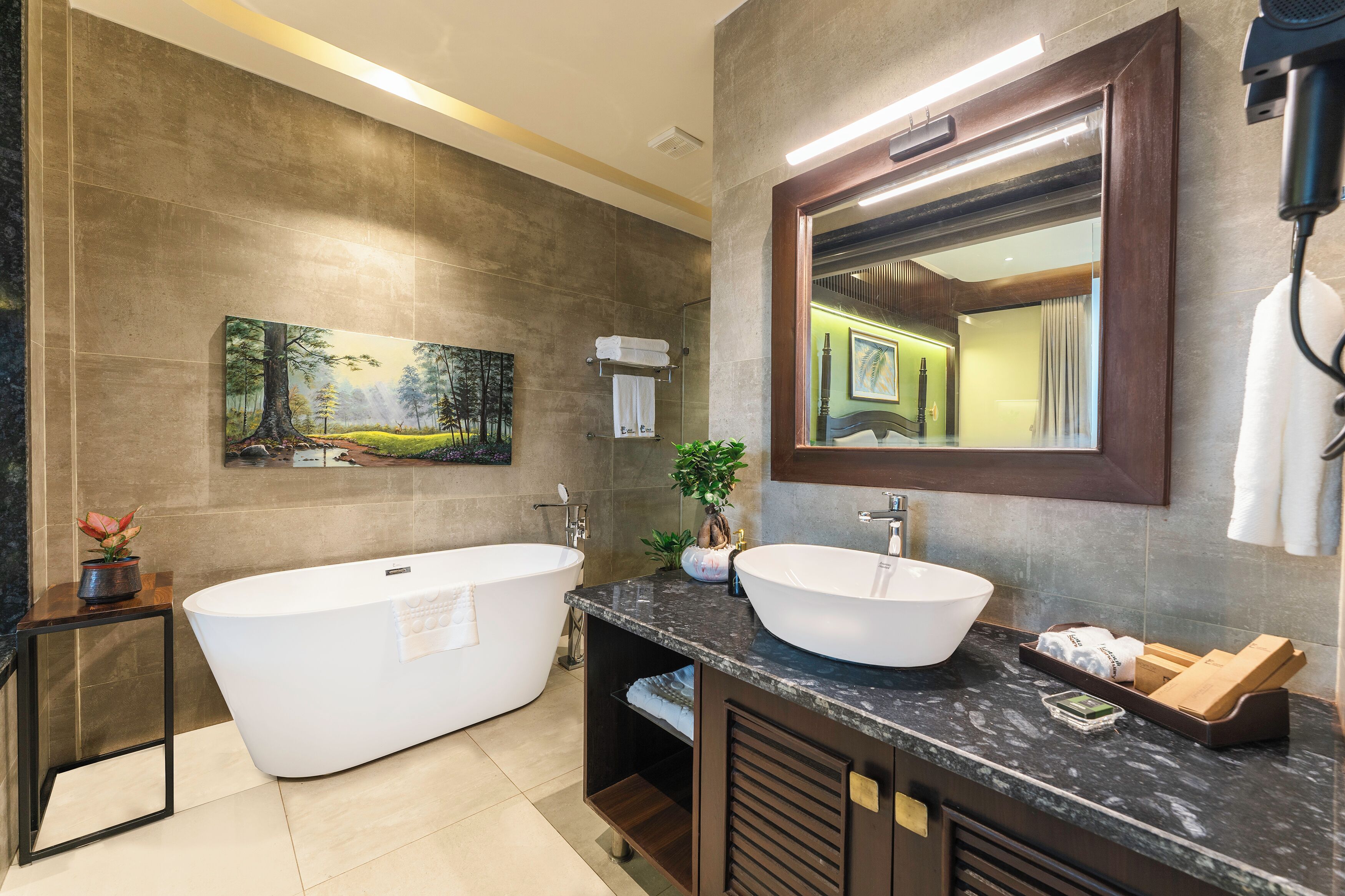 A modern bathroom with a freestanding bathtub, a large sink, a mirror, and a painting on the wall.