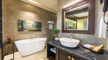 A modern bathroom with a freestanding bathtub, a large sink, a mirror, and a painting on the wall.