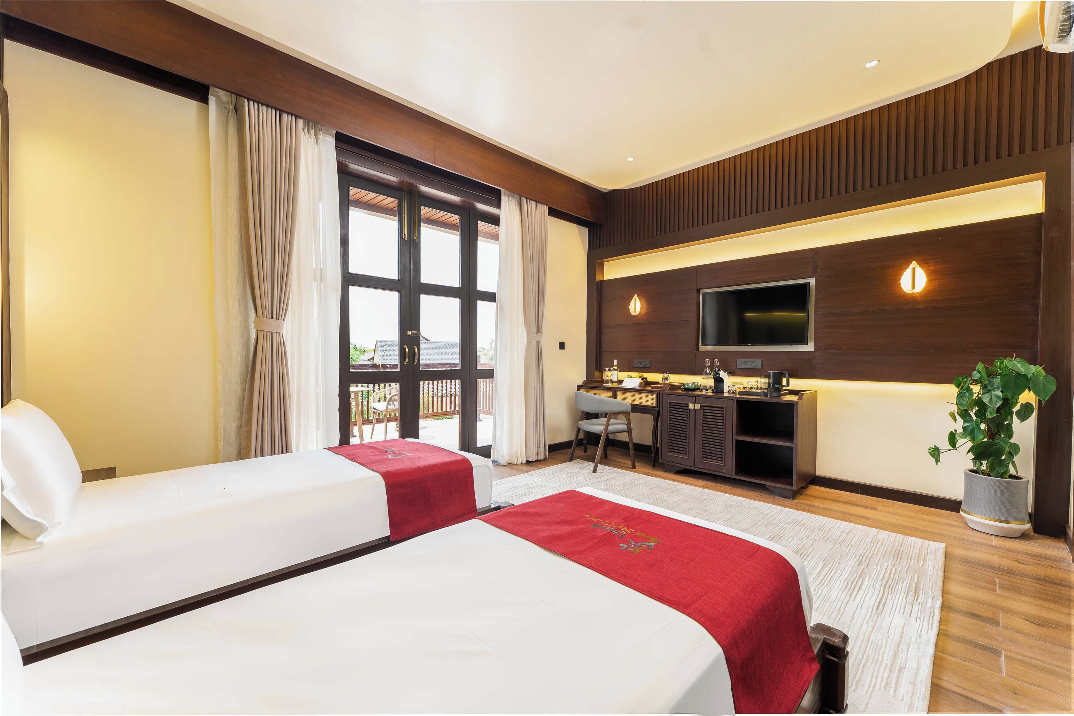 A hotel room with two beds, a desk, a TV, and a potted plant.