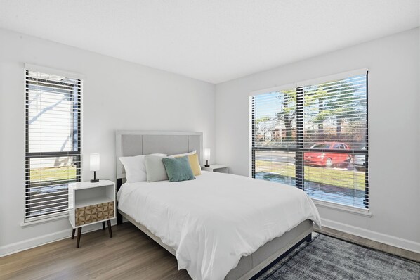 A bedroom with a bed, nightstands, and a window with blinds. - Modern Ease at The Taylor (Louisville)