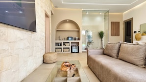 A modern living room with a glass coffee table, a sofa, and a built-in kitchen area with appliances. - Bungalow Palmeraie-Heated swimming pool not overlooked (Marrakech)