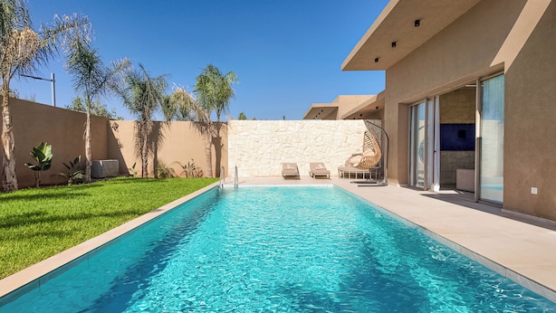 A swimming pool with two lounge chairs and a stone wall in the background. - Bungalow Palmeraie-Heated swimming pool not overlooked (Marrakech)