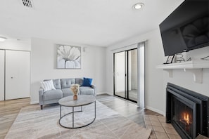 A modern living room with a grey sofa, a coffee table, a fireplace, and a large window. - Your Modern Escape at 502 (Louisville)