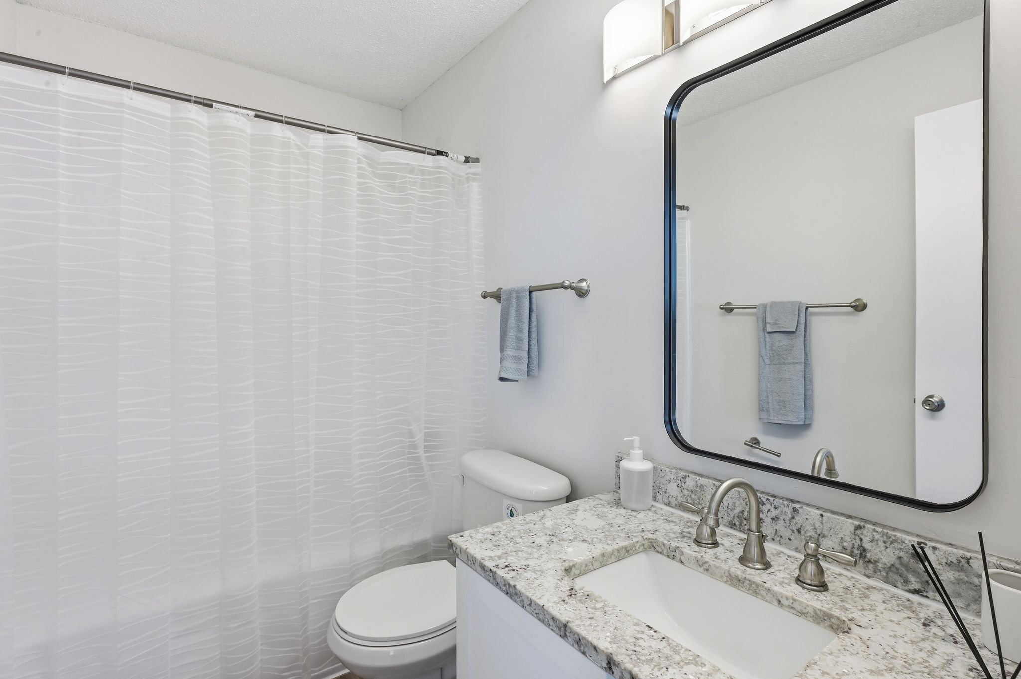 A bathroom with a shower, toilet, sink, and a large mirror.