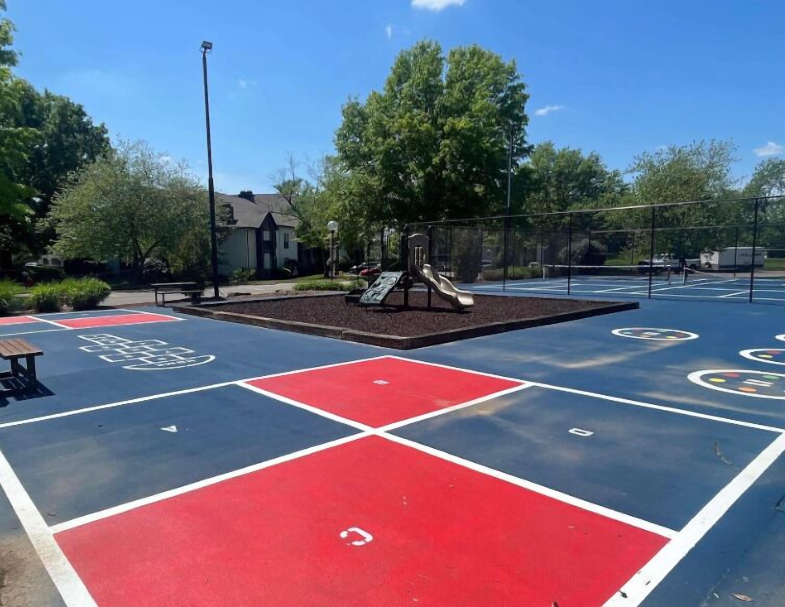 A playground with a slide and a basketball court with red and blue sections.