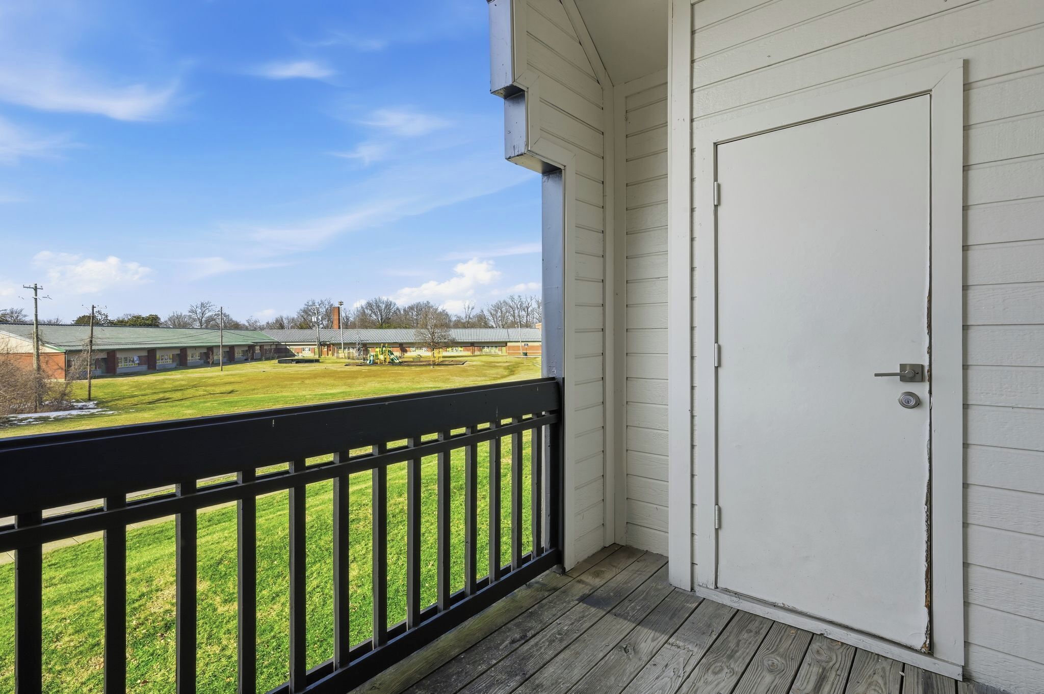 A balcony with a view of a grassy area and a building in the background.