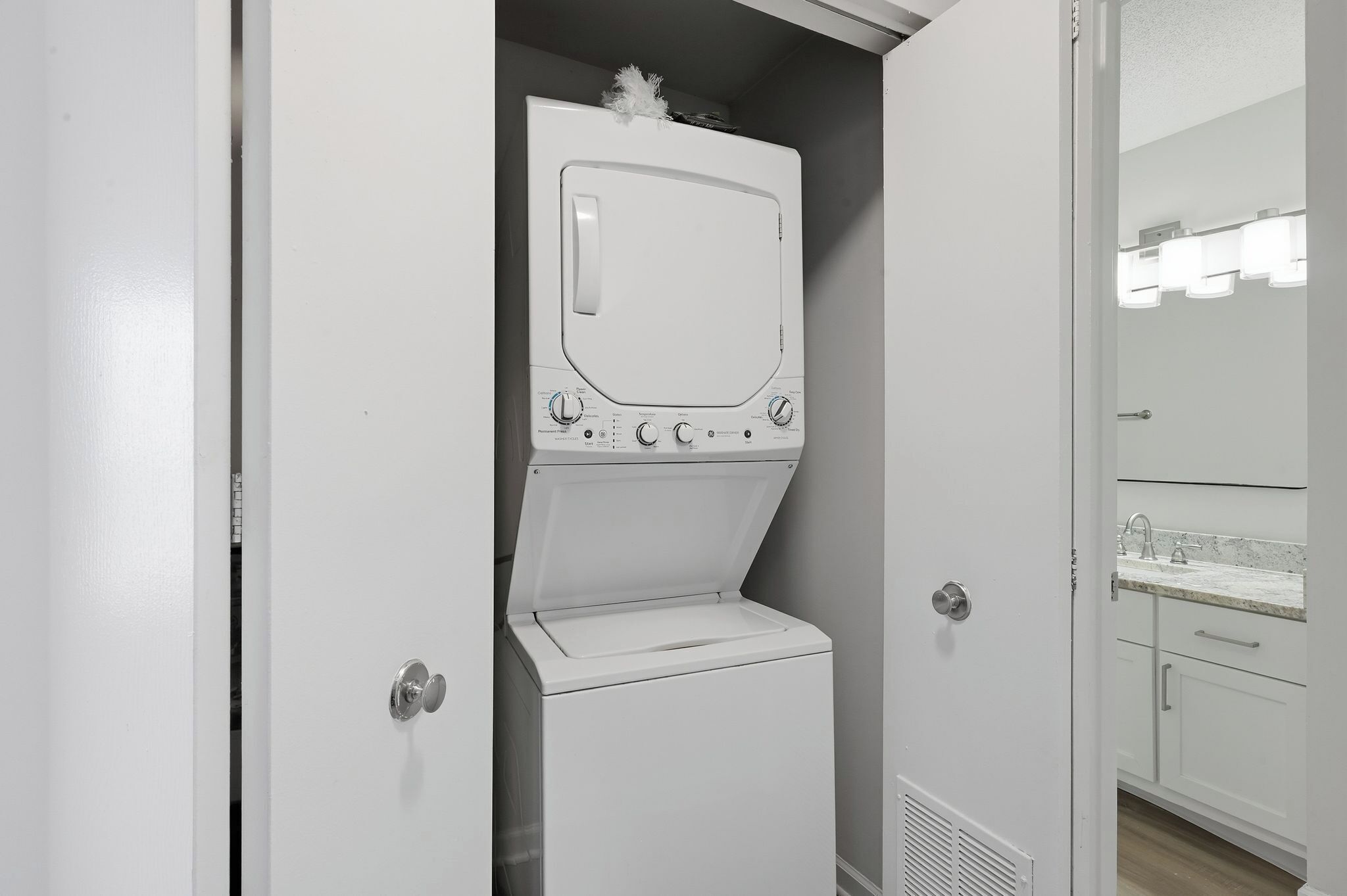 Een kleine, witte wasruimte met een ingebouwde wasmachine en droger, een spiegel en een wastafel met aanrecht.