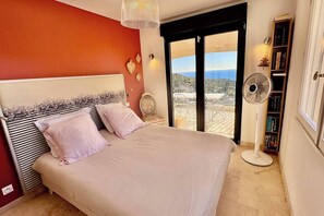 Une chambre avec un lit, un ventilateur, une bibliothèque et une vue sur l’extérieur.