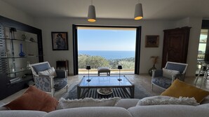 En stue med et glasbord, to lænestole, en sofa og udsigt til havet.