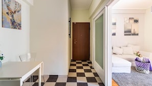 En hall med ett rutmönstrat golv, en dörr, en vit soffa och en tavla på väggen.