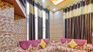 A living room with two floral sofas, a red coffee table, and patterned walls. - M K Hotel And Restaurant (Jammu)