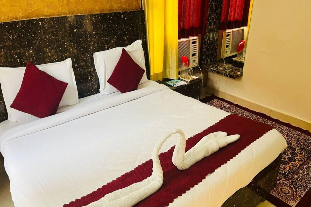 Una cama bien hecha con una colcha blanca y roja, dos almohadas y una toalla decorativa con forma de cisne.