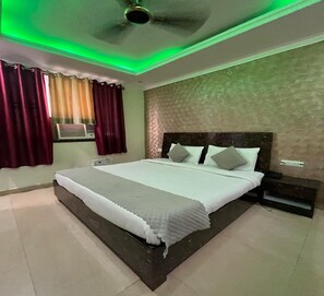 A bedroom with a large bed, a ceiling fan, and a window with curtains. - M K Hotel And Restaurant (Jammu)