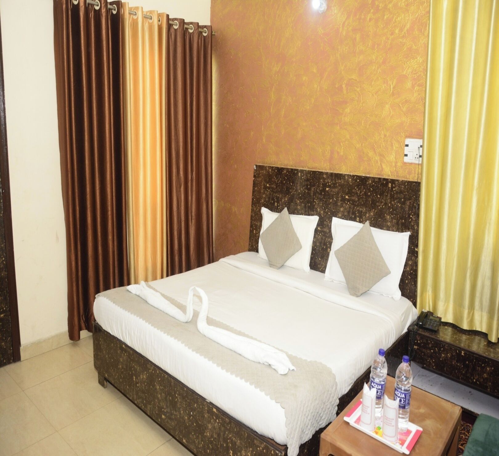 A hotel room with a large bed, a wooden headboard, and a nightstand with water bottles.