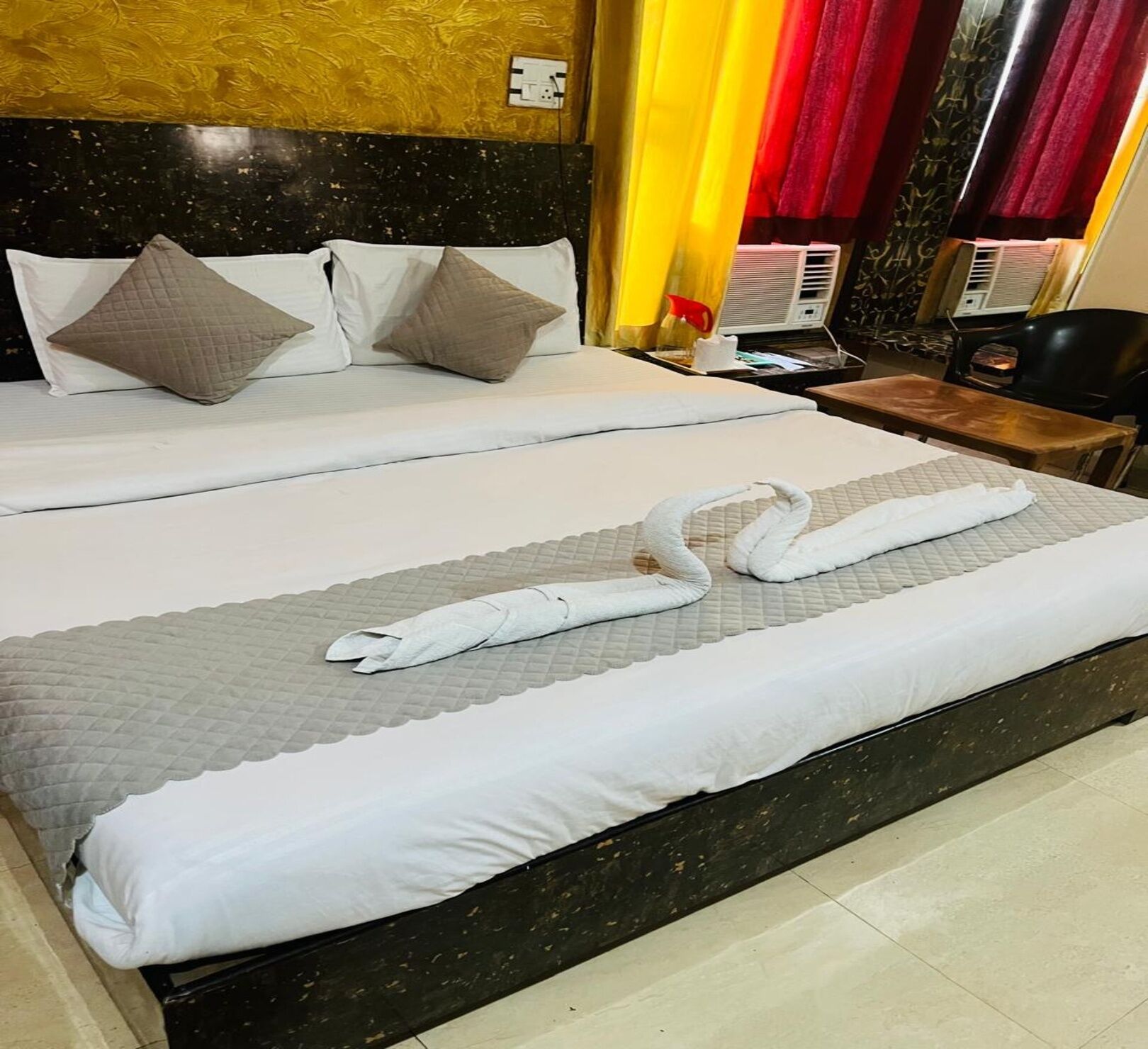 A hotel room with two beds, a marble headboard, and a small table with a chair.