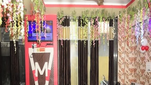 A restaurant with tables and chairs, a TV screen, and hanging plants. - M K Hotel And Restaurant (Jammu)