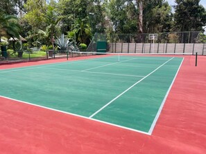 An outdoor tennis court with a green playing surface and red surrounding area.
