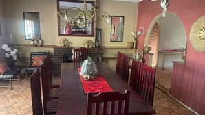Une salle à manger avec une longue table, des chaises, un lustre et une cheminée en briques.