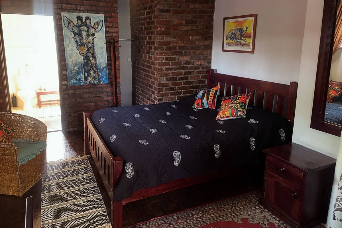 A bedroom with a wooden bed, a brick wall, and a painting of a giraffe.