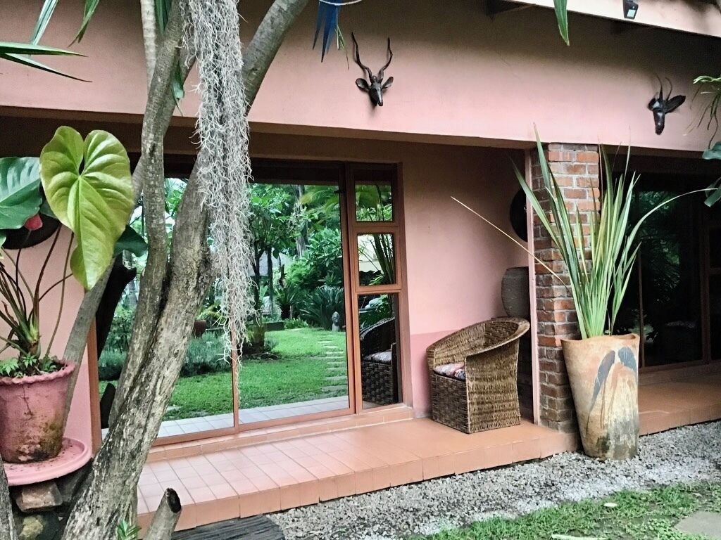 Ein Gebäude mit einer rosafarbenen Fassade, großen Fenstern und einer kleinen Veranda mit Korbmöbeln.