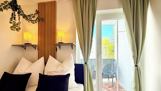 Una camera d'albergo con un letto, due lampade ai comodini, vista su un balcone esterno e una porta che conduce al balcone.