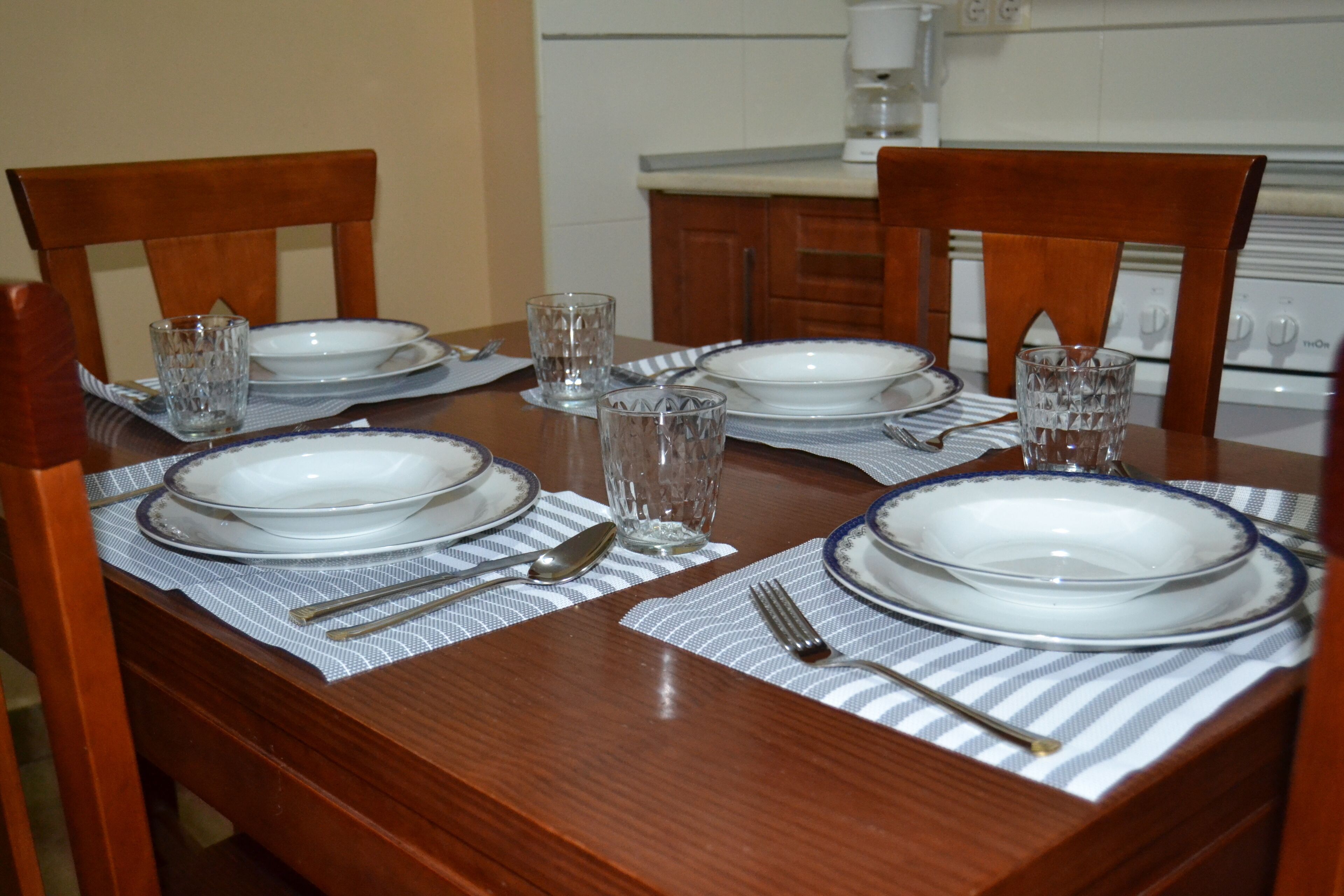 Een eettafel gedekt met borden, glazen, bestek en placematen in een keuken.