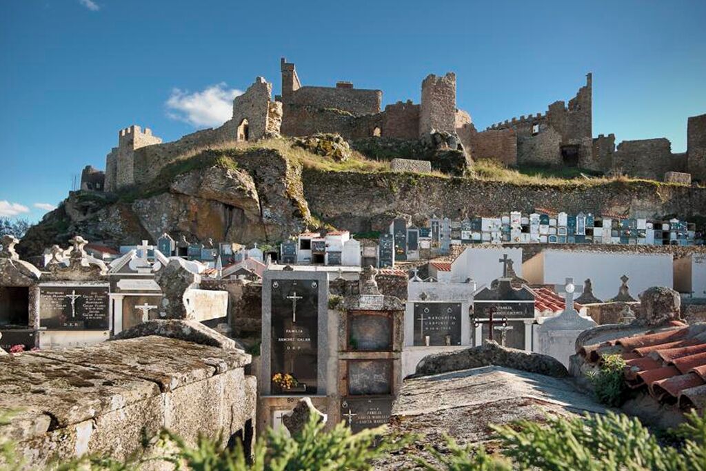 Un cementerio con lápidas y un castillo histórico al fondo.