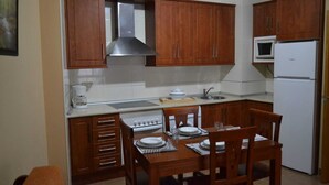 A compact kitchen with wooden cabinets, a stainless steel range hood, a microwave, and a refrigerator. There is a dining table with chairs and a coffee maker. - Hostal Ruralis Altozano  (Montánchez)