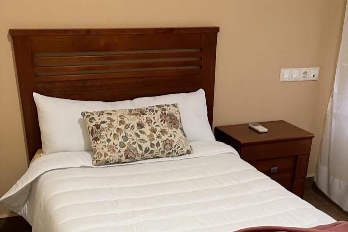 A neatly made bed with a wooden headboard, a patterned pillow, and a brown blanket.