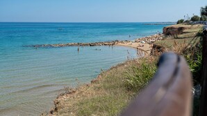 Strandudsigt med klart vand, klippefyldt kystlinje og enkelte badegæster.