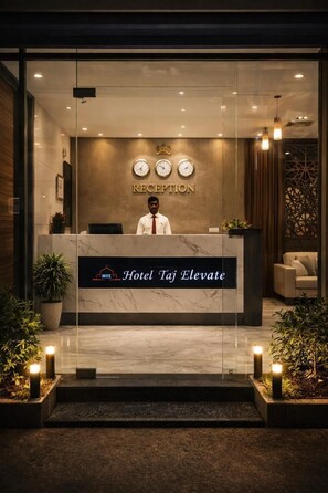 A reception desk at Hotel Taj Elevate with a receptionist, a clock, and a sign indicating the reception area. - Hotel Taj Elevate  (Agra)
